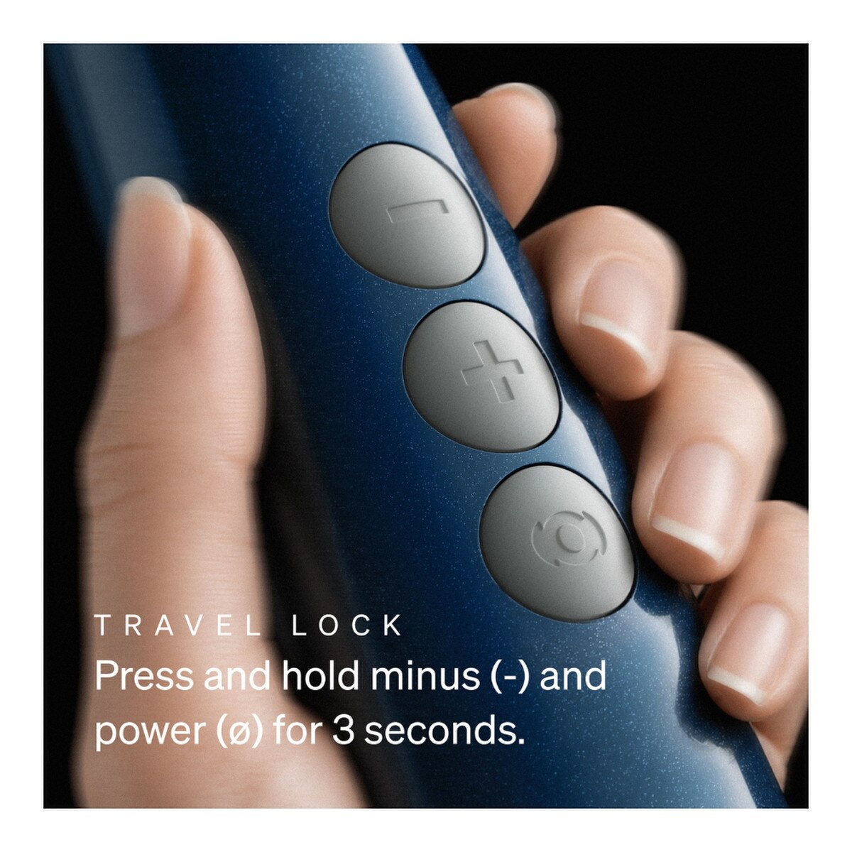 Close-up of a hand holding a dark blue Doxy Wand demonstrating the travel lock remote control, showing three gray buttons with minus, plus, and power symbols. White text at the bottom reads: 'TRAVEL LOCK: Press and hold minus (-) and power (o) for 3 seconds - Adult Toys - Vibrators - Wands - Danish Blue Adult Centres